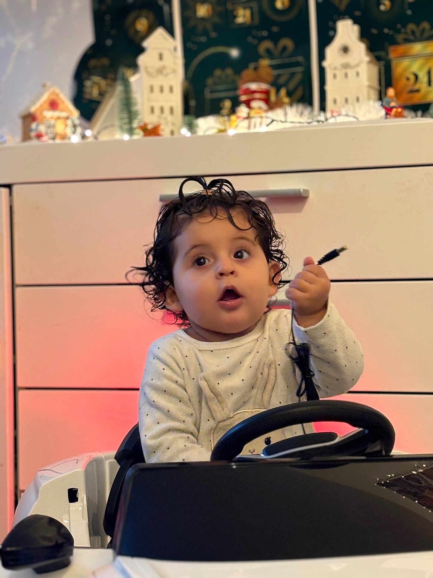 Dynna Authier a rejoint le concours — aidez-le/la à gagner de superbes lots ! child, toddler, baby, curly_hair, surprised_face, mouth_open, hand, cable, steering_wheel, toy_car, indoor, dresser, holiday_decor, christmas_village, festive_lights, onesie, polka_dots, seat, portrait, soft_lighting