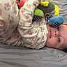 Kenzley is registered to the contest to win money with this photo: baby, pajamas, bed, plush_toy, child, face, sleepwear, infant, cute, lying_down, soft_toy, patterned_clothing, indoors, resting, young_child, portrait, cozy, looking, head, comfort