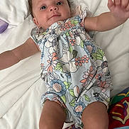 Kenzley joined the competition — help win amazing prizes! baby, infant, child, romper, floral_pattern, bed, white_bedding, cute, smiling, reaching_hand, person, young_child, lying_down, skin, face, blue_eyes, short_hair, indoors, colorful_clothing, playful