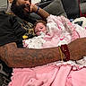 man, baby, blanket, pacifier, tattoo, bracelet, couch, pillow, person, indoor, relaxing, family, love, comfort, casual, beard, clothing, home, portrait, cozy