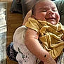 baby, smiling, yellow_clothing, arm, blanket, indoor, wooden_floor, person_holding, infant, happy, peaceful, sleepy, skin, human, closeup, portrait, newborn, cute, resting, warm_light