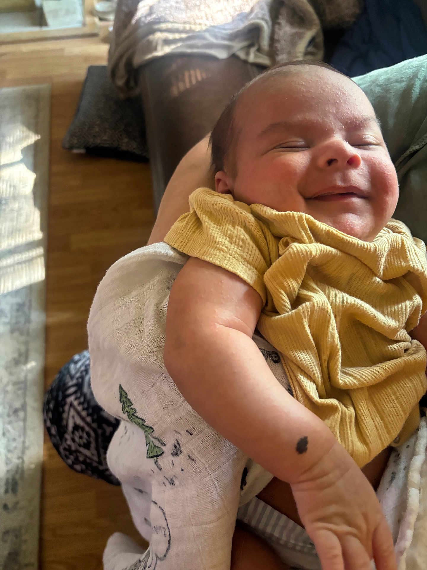 Jevonne is registered to the contest to win money with this photo: baby, smiling, yellow_clothing, arm, blanket, indoor, wooden_floor, person_holding, infant, happy, peaceful, sleepy, skin, human, closeup, portrait, newborn, cute, resting, warm_light