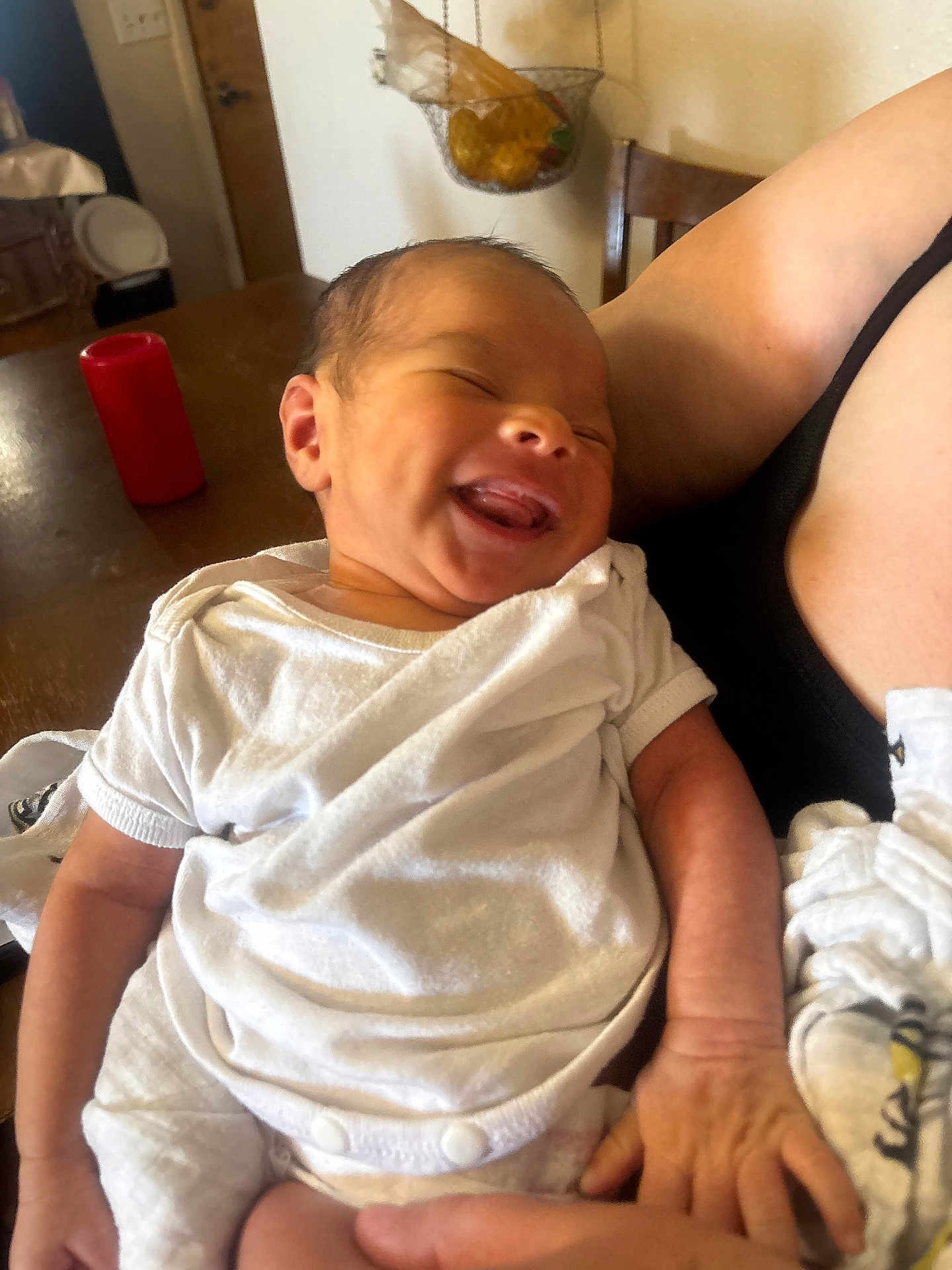 Jevonne is registered to the contest to win money with this photo: baby, newborn, smile, white_clothing, infant, arm, hand, indoor, table, candle, fruit_basket, wooden_chair, person, holding, happy, closeup, skin, relaxation, family, care