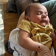 Jevonne is registered to the contest to win money with this photo: baby, sleeping, yellow_clothing, infant, arm, blanket, indoor, person, skin, peaceful, resting, cozy, home, soft_light, wood_floor, fabric, closeup, newborn, comfort, child
