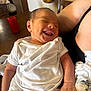 Deliah is registered to the contest to win money with this photo: baby, newborn, smile, white_clothing, infant, arm, hand, indoor, table, candle, fruit_basket, wooden_chair, person, holding, happy, closeup, skin, relaxation, family, care