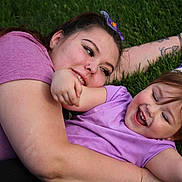 Deliah is registered to the contest to win money with this photo: child, woman, grass, laughing, hug, purple_clothing, flower_accessory, happy, outdoor, playful, smiling, casual, nature, family, affection, skin, person, head, arm, tattoo