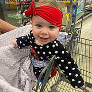 Gabriella joined the competition — help win amazing prizes! aisle, baby, blanket, child, clothing, cute, face, floor, happy, indoor, metal_cart, person, polka_dot, red_headband, retail, seat_belt, shopping_cart, smile, store, supermarket
