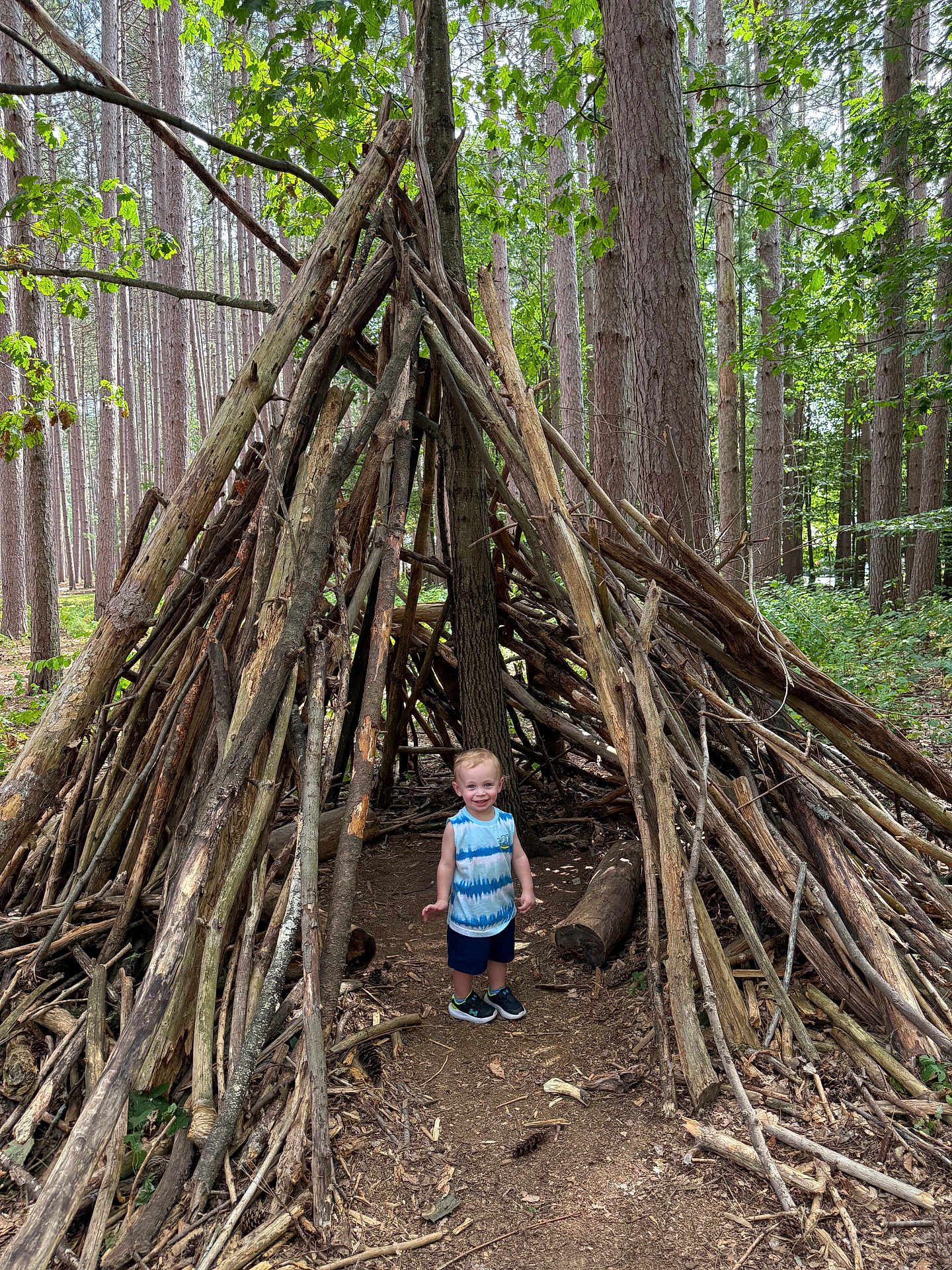 Colin joined the competition — help win amazing prizes! child, toddler, forest, trees, sticks, teepee, wood, nature, outdoor, play, adventure, smile, path, greenery, sunlight, leaves, shoes, tank_top, shorts, happy