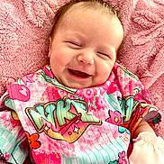 Paisley is registered to the contest to win money with this photo: baby, newborn, infant, smiling, portrait, close_up, face, happy, sleepy, pink_blanket, colorful_clothing, patterned_outfit, mittens, gummy_smile, lying_down, cozy, indoors, soft_blanket, head, child
