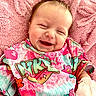 baby, newborn, infant, smiling, portrait, close_up, face, happy, sleepy, pink_blanket, colorful_clothing, patterned_outfit, mittens, gummy_smile, lying_down, cozy, indoors, soft_blanket, head, child