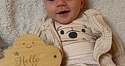 Aaron a rejoint le concours — aidez-le/la à gagner de superbes lots ! baby, infant, smile, clothing, blanket, wooden_sign, cute, cozy, happy, face, socks, sitting, child, portrait, indoor, soft_texture, warm_colors, person, candid, cute_expression