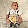 baby, infant, smile, sitting, clothing, socks, suspenders, wooden_sign, fluffy_blanket, heart_pillow, cute, portrait, indoor, soft_texture, happy, face, skin, hand, footwear, young_child
