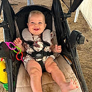 Fletcher is registered to the contest to win money with this photo: baby, stroller, child, smile, happy, blue_eyes, plastic_toys, outdoor, sand, seatbelt, infant, clothing, cute, person, legs, feet, mesh_canopy, play, joy, sunlight