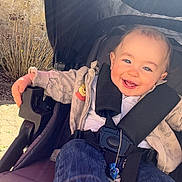 Tyron participe au concours pour gagner de l'argent avec cette photo : baby, bushes, casual, child, cute, denim_pants, face, happy, head, jacket, nature, outdoor, person, seatbelt, smiling, stone_wall, striped_socks, stroller, sunlight, winnie_the_pooh