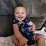 baby, smiling, happy, infant, child, onesie, floral_pattern, couch, furniture, indoors, skin, hand, foot, hair, person, sitting, blanket, cute, portrait, expression