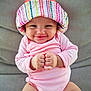 baby, infant, smiling, hat, colorful, pink_onesie, fists, cute, child, portrait, seated, indoors, cushion, comfort, happy, face, headwear, skin, person, expression