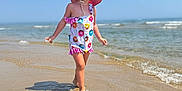 Lya a rejoint le concours — aidez-le/la à gagner de superbes lots ! child, beach, ocean, water, sand, sunhat, sunglasses, swimsuit, summer, sunny, walking, waves, shoreline, outdoor, vacation, playful, cute, young, fun, daytime