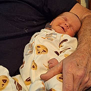 Emma is registered to the contest to win money with this photo: baby, infant, newborn, sleeping, smiling, pajamas, cookie_pattern, footed_pajamas, hand, adult_arm, holding, cozy, closeup, portrait, indoor, bedding, furniture, fabric, skin, affectionate