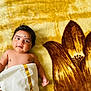 baby, infant, child, blanket, floral_pattern, yellow, brown, cloth, wrapped, lying_down, cute, portrait, skin, face, expression, indoors, soft_texture, newborn, small_hand, curly_hair