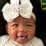 baby, child, face, headband, bow, bunny_ears, smile, tongue, cute, infant, closeup, portrait, happy, apparel, white_clothing, dark_background, expression, adorable, young, person