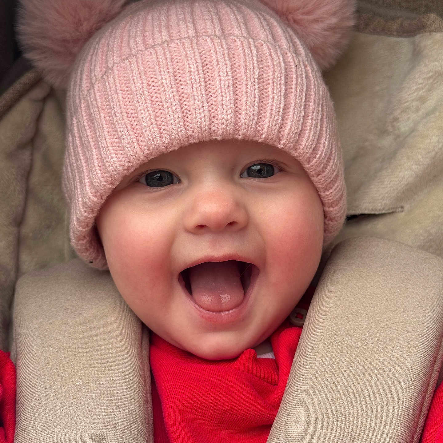 Verity joined the competition — help win amazing prizes! adorable, baby, car_seat, cheerful, child, closeup, cute, face, happy, headwear, infant, knitwear, pink_hat, pom_poms, portrait, red_clothing, seatbelt, smiling, warm_clothing, young_child