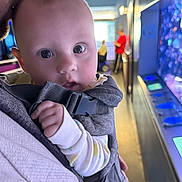 Verity joined the competition — help win amazing prizes! baby, infant, adult, baby_carrier, close_up, indoor, person, face, hand, clothing, blurred_background, blue_lighting, gentle_kiss, parent, bonding, human, carrier_strap, soft_light, curious_expression, casual_wear
