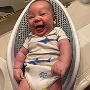 Weston is registered to the contest to win money with this photo: baby, infant, smiling, onesie, shark_pattern, fish_pattern, baby_bath_seat, bathroom, tile_floor, happy, cute, child, skin, hand, leg, sitting, indoor, plump, chubby, joyful