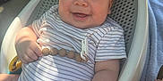 Weston is registered to the contest to win money with this photo: baby, smiling, striped_onesie, baby_seat, beaded_toy, happy, infant, outdoor, sunlight, shadow, skin, person, cute, chubby, relaxed, seat, plastic, hand, foot, daylight
