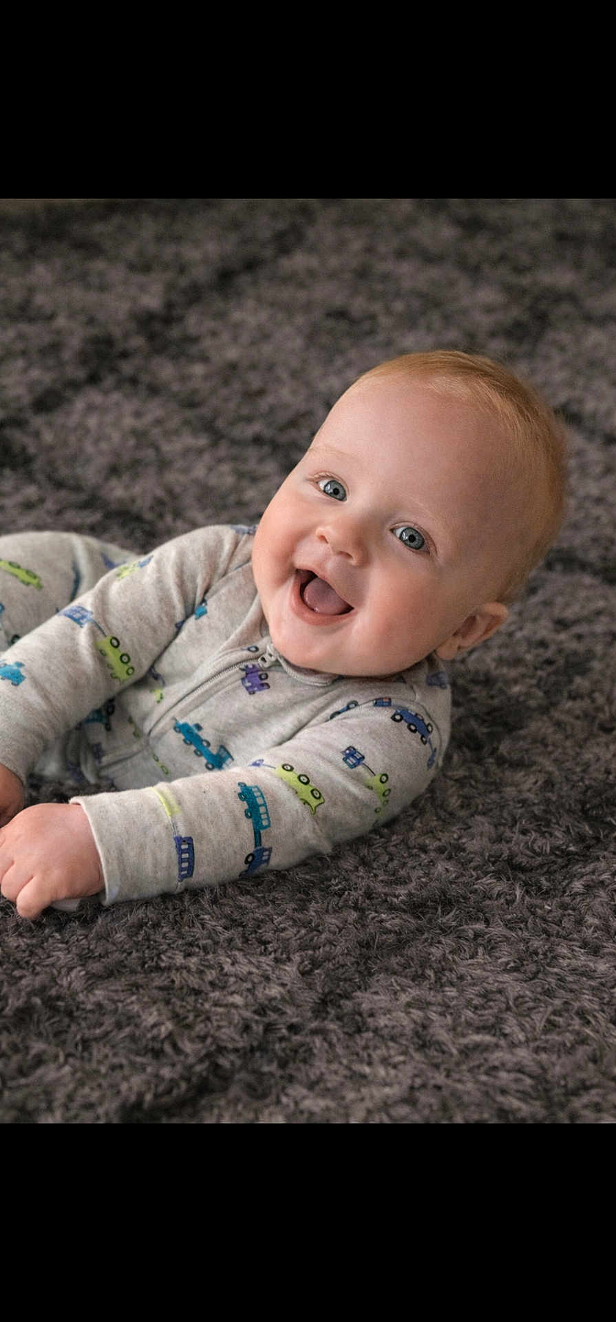 Greyson is registered to the contest to win money with this photo: baby, child, smiling, onesie, blue_eyes, car_prints, carpet, soft_texture, happy, infant, cute, portrait, indoors, laying_down, cozy, young, skin, face, hands, expression