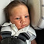 baby, infant, car_seat, safety_harness, seat_belt, white_shirt, blue_eyes, close_up, child, head_support, serious_expression, hair, fabric, padding, infant_seat, person, portrait, seat, straps, clothing