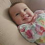 baby, infant, smiling, tongue_out, floral_clothing, cute, face, child, portrait, closeup, soft_texture, cushion, happy, indoors, young_child, cozy, sleepwear, resting, warm_colors, cheerful
