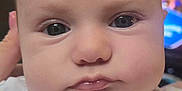 Peyton is registered to the contest to win money with this photo: baby, close_up, face, infant, child, eyes, lips, hand, skin, clothing, patterned_outfit, floral, indoor, portrait, cute, young, person, newborn, expression, soft_lighting