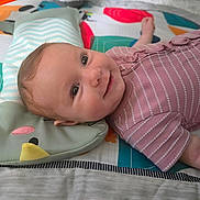 Peyton is registered to the contest to win money with this photo: baby, infant, smile, face, child, lying_down, pillow, animal_pillow, colorful, patterned_mat, clothing, pink_shirt, happy, cute, indoors, soft_lighting, closeup, portrait, young_child, cozy