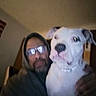 Izzie is registered to the contest to win money with this photo: person, dog, indoor, hoodie, glasses, white_dog, pet, portrait, companion, blur, casual, face, animal, friendly, man, domestic_animal, collar, closeup, bond, house
