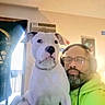 Izzie is registered to the contest to win money with this photo: dog, man, indoor, headphones, glasses, neon_hoodie, white_dog, black_markings, air_conditioner, door, light, casual, relaxed, pet, companion, portrait, seated, home, beard, furniture