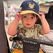 Emmanuel a rejoint le concours — aidez-le/la à gagner de superbes lots ! toddler, child, baby, cap, hat, animal_print, shirt, stroller, maxi_baby, yellow_shorts, indoor, curious, face, hands, seated, portrait, cute, looking_at_camera, playful, young_child