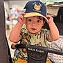 toddler, child, baby, cap, hat, animal_print, shirt, stroller, maxi_baby, yellow_shorts, indoor, curious, face, hands, seated, portrait, cute, looking_at_camera, playful, young_child