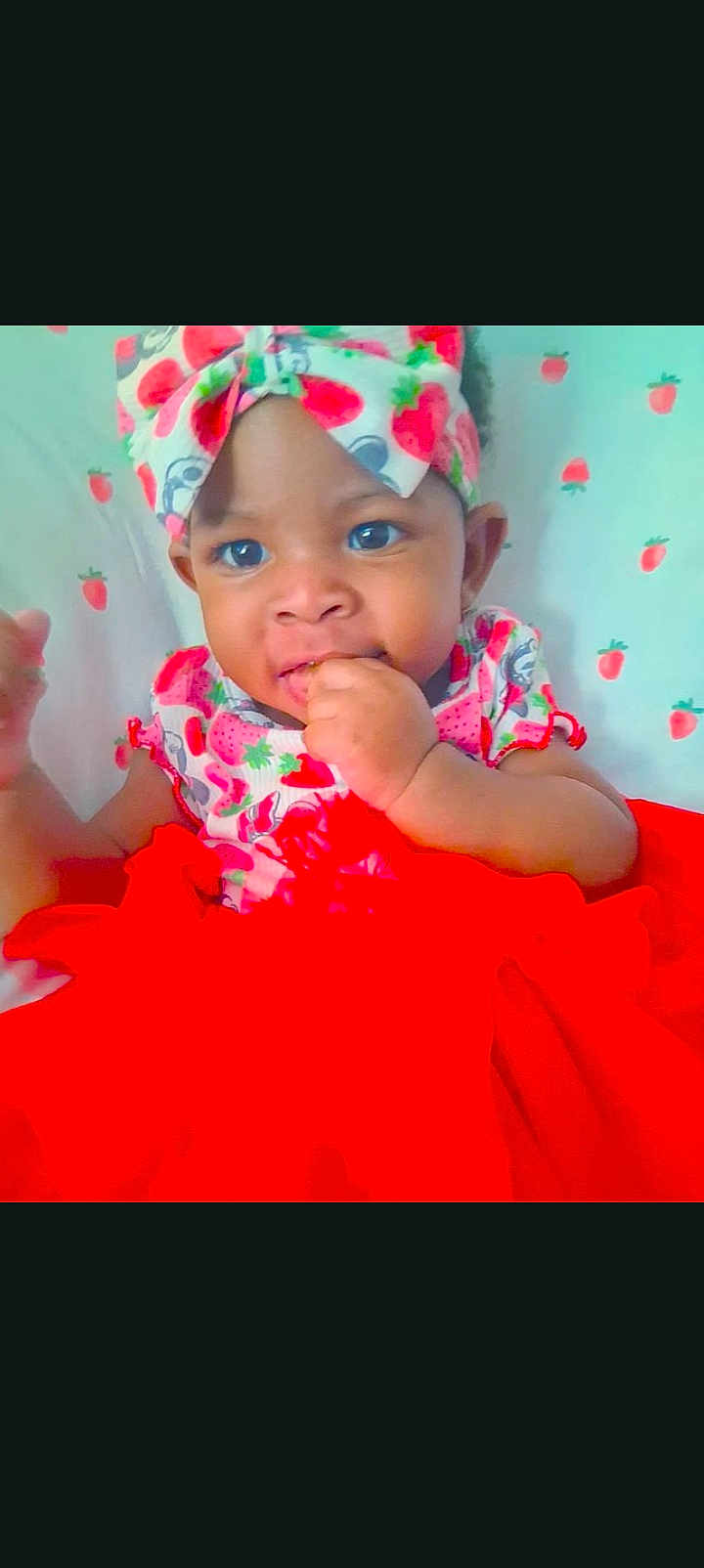 Saniyah Heaven joined the competition — help win amazing prizes! baby, infant, child, person, headband, strawberry_print, red_dress, tutu, hand_in_mouth, closeup, big_eyes, bed, bedding, patterned_background, bright_colors, smile, sitting, portrait, adorable, clothing