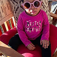 Saniyah Heaven joined the competition — help win amazing prizes! child, toddler, girl, sunglasses, headband, pink_shirt, long_sleeve, chair, cushion, outdoor, portrait, hands, shoes, socks, wooden_rail, patterned_pillow, sunlight, casual_clothing, playful, fashionable