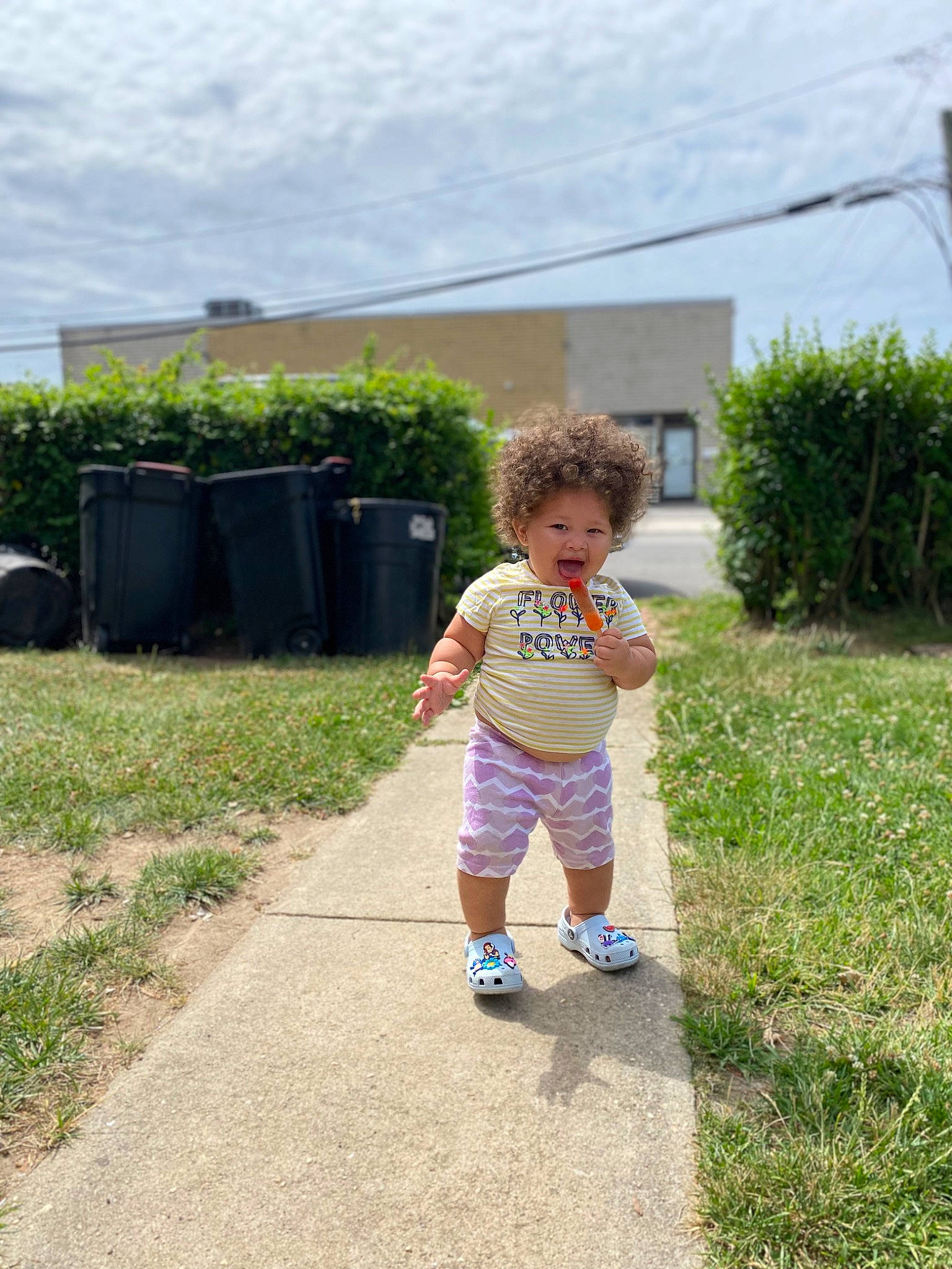 Alyssa is registered to the contest to win money with this photo: asphalt, cloud, garden, grass, grassland, house, landscape, lawn, leisure, people_in_nature, person, plant, recreation, road, road_surface, sandal, shorts, sky, soil, toddler