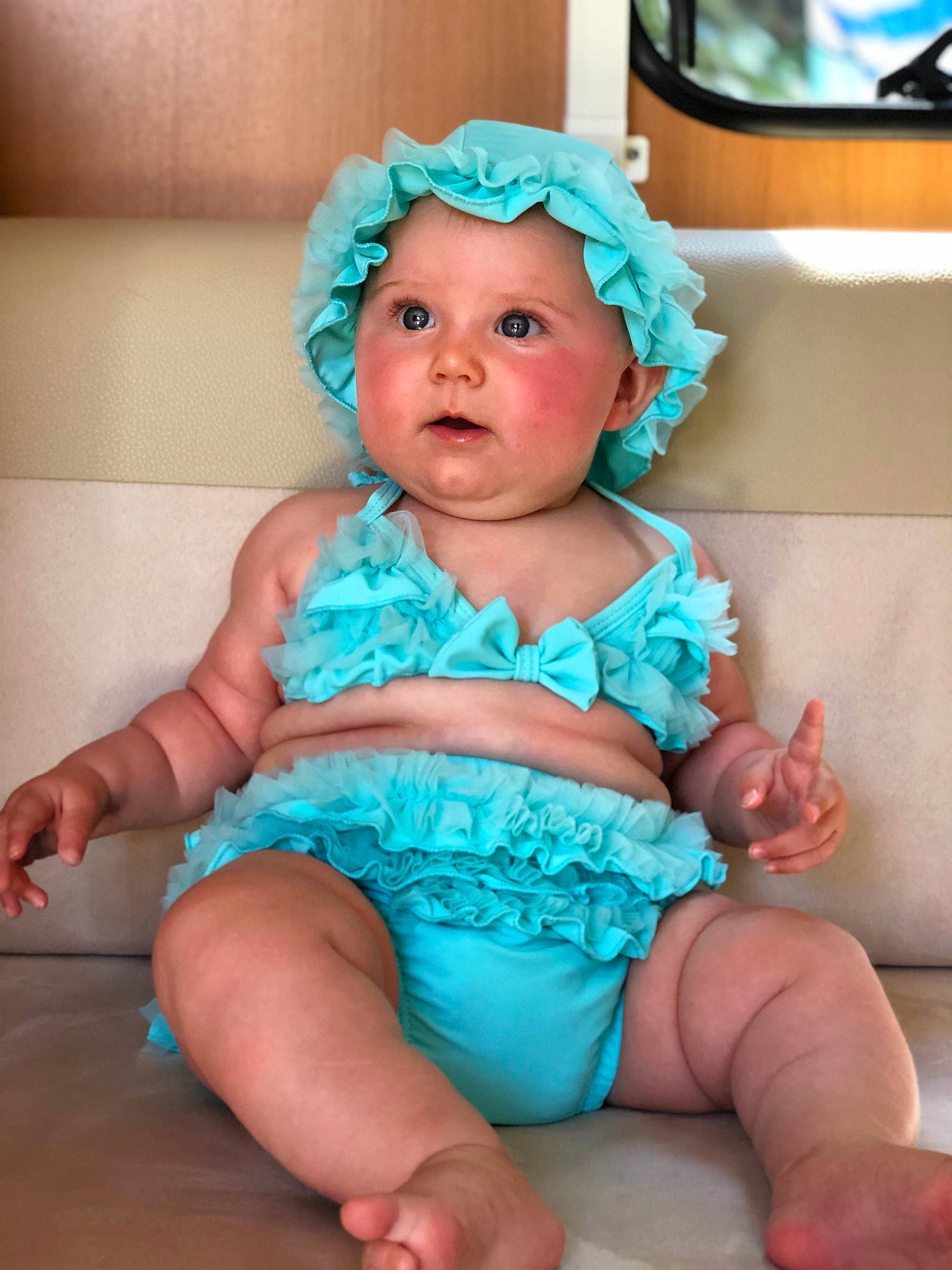Mia a rejoint le concours — aidez-le/la à gagner de superbes lots ! aqua, baby, baby_bloomers, baby_toddler_clothing, child, diaper, fashion_accessory, headgear, headwear, person, ruffle, sitting, smile, surprise, toddler, turquoise