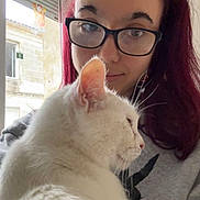 Whitesy participe au concours pour gagner de l'argent avec cette photo : person, cat, white_cat, glasses, indoor, window, natural_light, red_hair, long_hair, sweatshirt, pet, close_up, portrait, calm, cozy, feline, domestic_animal, cute, companion, relaxing