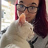 person, cat, white_cat, glasses, indoor, window, natural_light, red_hair, long_hair, sweatshirt, pet, close_up, portrait, calm, cozy, feline, domestic_animal, cute, companion, relaxing