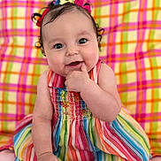 Zeina-Pierina joined the competition — help win amazing prizes! baby, child, smiling, colorful_dress, striped_dress, curly_hair, hair_bows, sitting, plaid_background, indoor, cute, happy, infant, portrait, person, skin, face, hand, foot, bright_colors