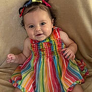 Zeina-Pierina is registered to the contest to win money with this photo: baby, child, smiling, rainbow_striped_dress, colorful_clothing, curly_hair, hair_bows, sitting, beige_blanket, happy, portrait, cute, infant, indoors, playful, young_child, person, bright_colors, closeup, expression