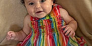 Zeina-Pierina is registered to the contest to win money with this photo: baby, beige_blanket, bright_colors, child, closeup, colorful_clothing, curly_hair, cute, expression, hair_bows, happy, indoors, infant, person, playful, portrait, rainbow_striped_dress, sitting, smiling, young_child