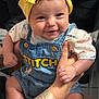 baby, child, smile, denim_overalls, yellow_headband, cute, hands, holding, happy, infant, face, person, clothing, indoor, portrait, young_child, sitting, casual_wear, bright, closeup