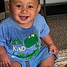 baby, infant, child, smiling, happy, sitting, portrait, indoors, blue_shirt, dinosaur_shirt, carpet, rug, furniture, home, floor, barefoot, baby_teeth, looking_at_camera, playful, close_up