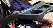 Jahmari joined the competition — help win amazing prizes! baby, child, stroller, outdoor, sitting, curious, profile, face, eyes, short_hair, blue_shirt, shorts, toy, blanket, snack_tray, grass, sidewalk, sunlight, portrait, infant