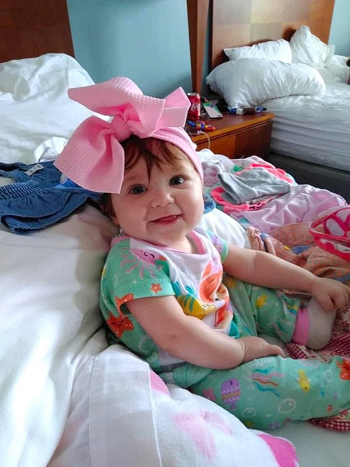 Payton is registered to the contest to win money with this photo: baby, baby_toddler_clothing, child, comfort, event, eye, fashion_accessory, fun, happy, hat, headwear, lamp, linens, magenta, person, pink, room, sitting, skin, smile
